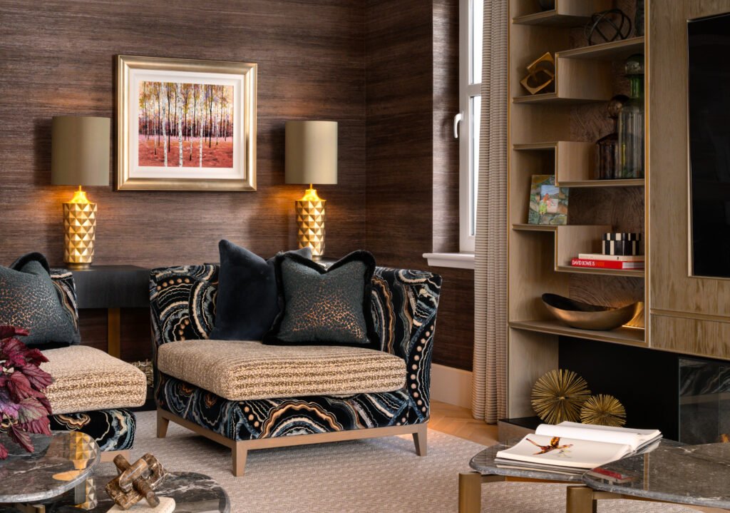Elegant living room with unique patterned armchairs, dark textured walls, golden lamps, birch tree art, and light wood shelving.